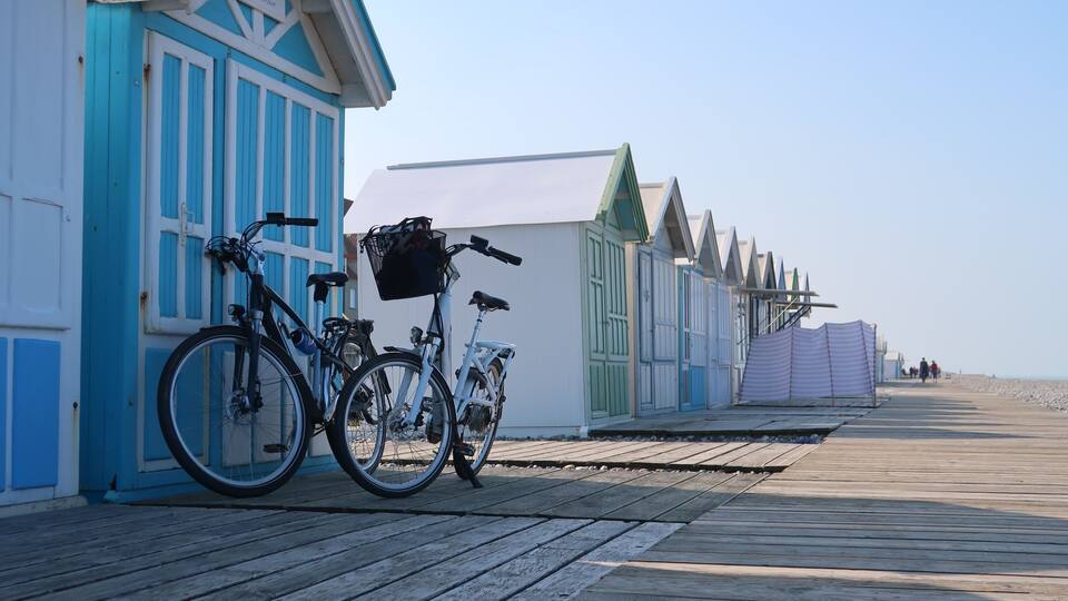 A wooden boardwalk with bicycles parked by a row of colorful beach huts.