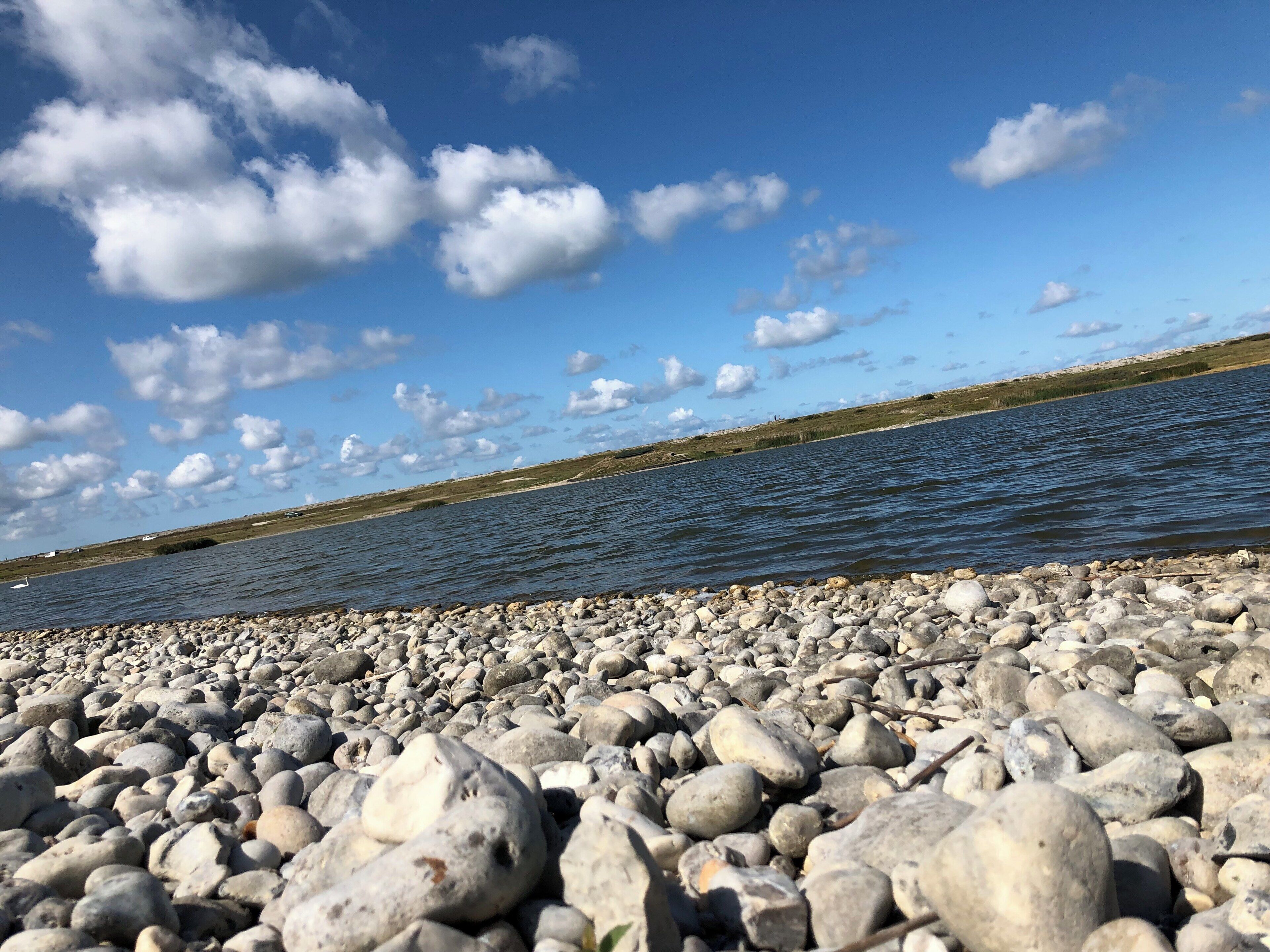 A rocky shoreline with a calm body of water and a clear sky with scattered clouds.