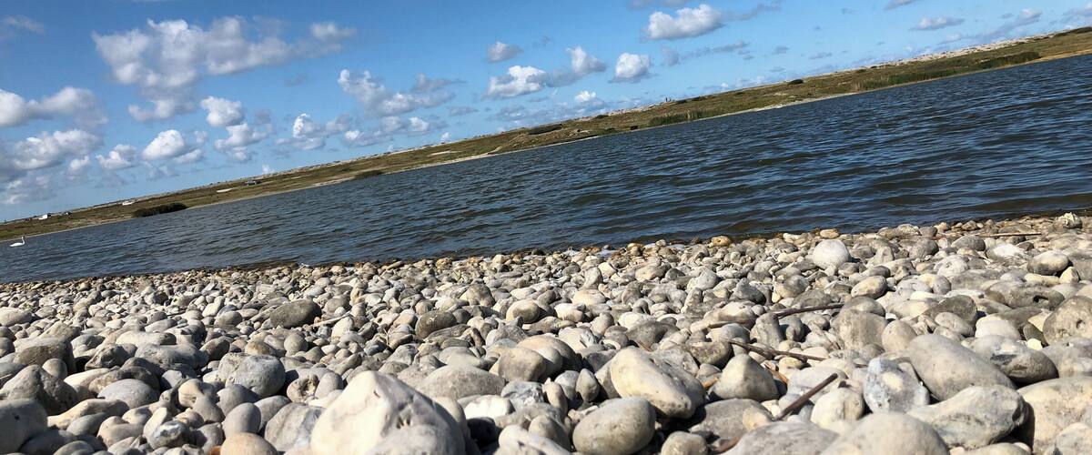 A rocky shoreline with a calm body of water and a clear sky with scattered clouds.