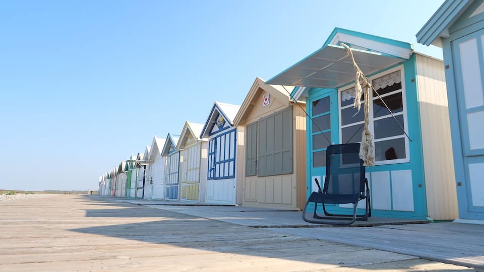 A row of colorful beach huts with a wooden boardwalk in front.