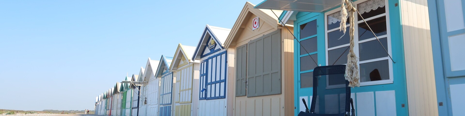 Uma fileira de cabanas coloridas à beira-mar, com uma passarela de madeira na frente.