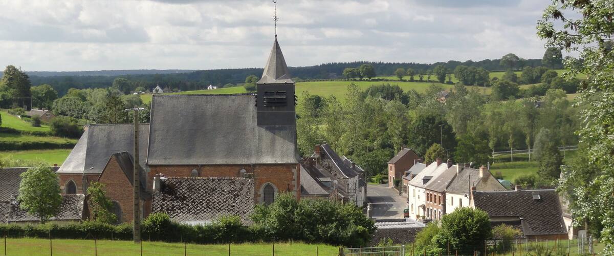 A church with a steeple and a bell tower, surrounded by green fields and trees.
