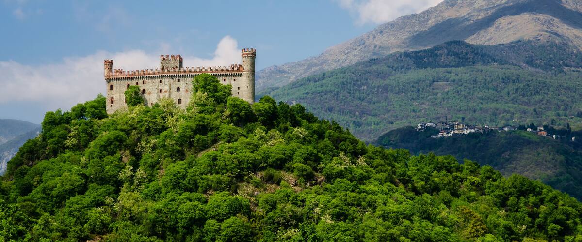 A castle on a hill with lush greenery and mountains in the background.