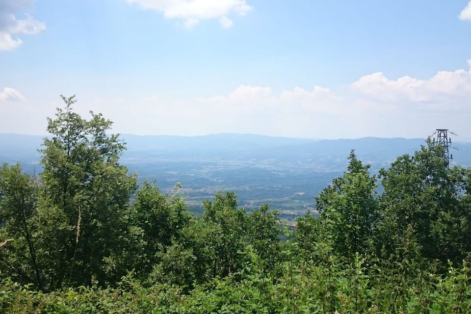 Un paisaje montañoso con vegetación verde y densa en primer plano y vistas de colinas distantes bajo un cielo despejado.