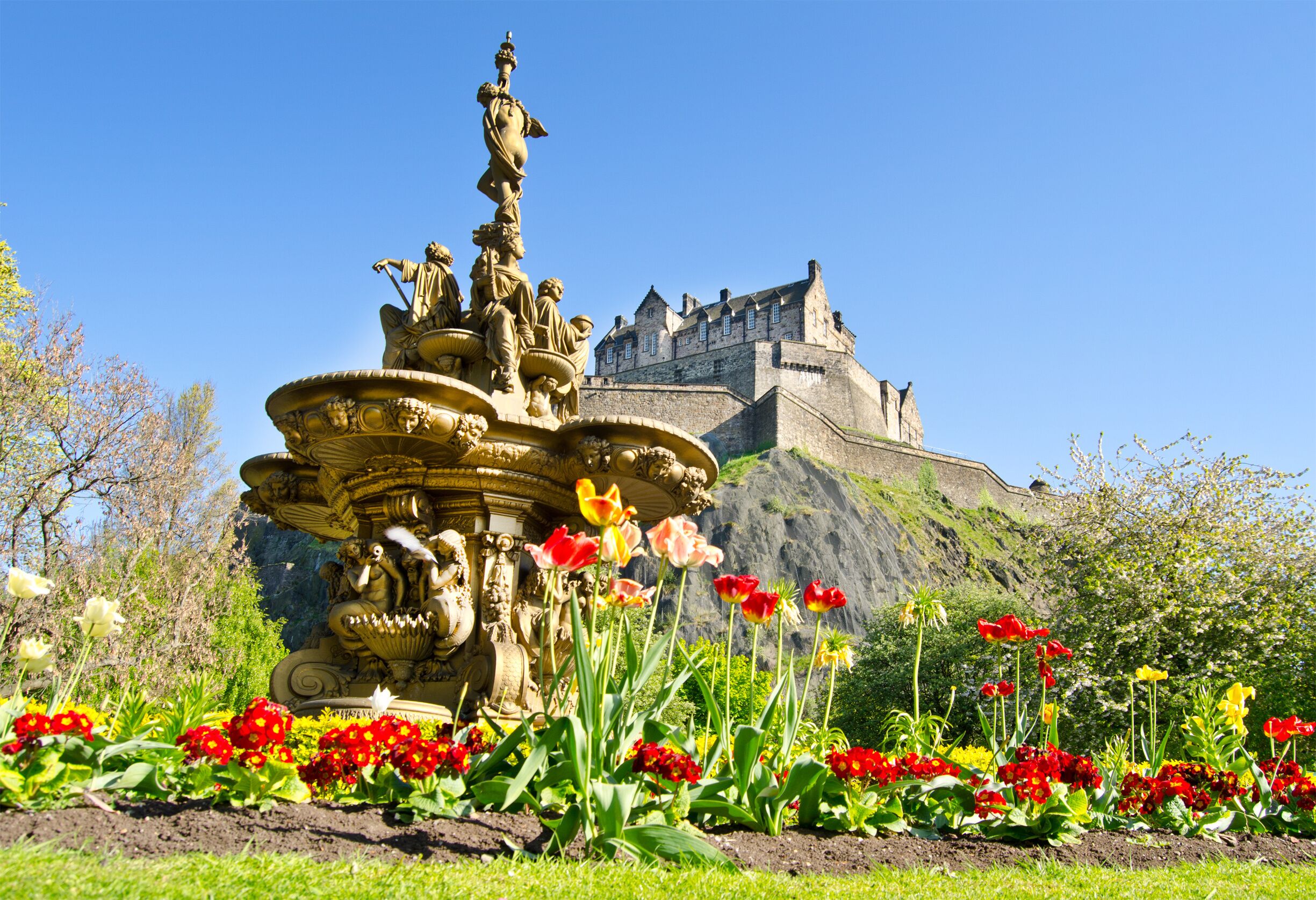 A historic castle on a hill with a fountain in the foreground.