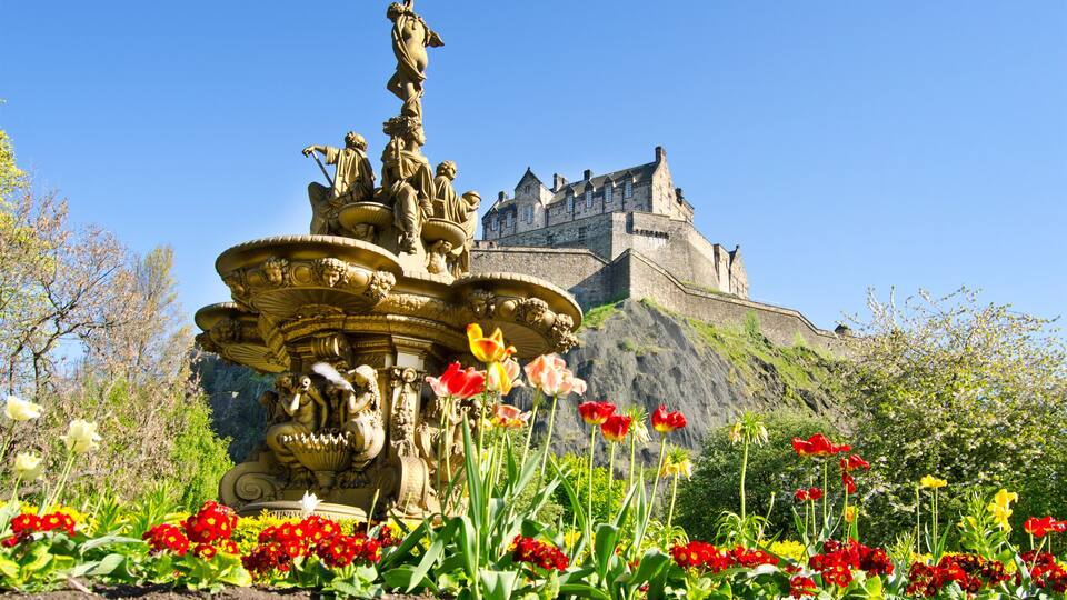 A historic castle on a hill with a fountain in the foreground.