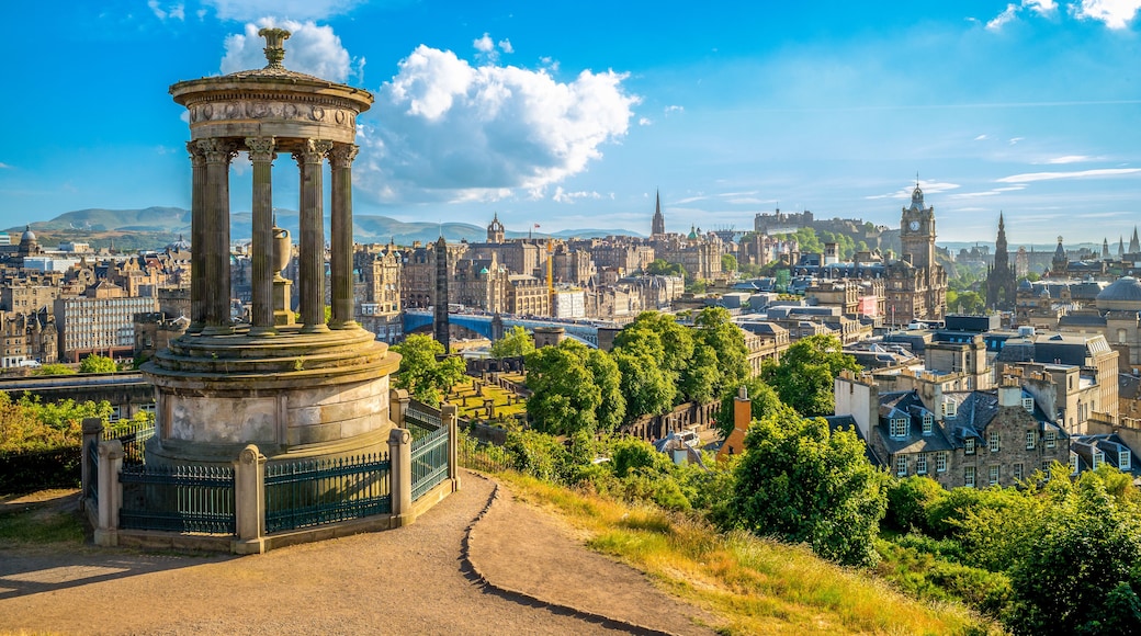 Um monumento histórico com colunas, uma paisagem urbana com diversos edifícios e um céu azul límpido.
