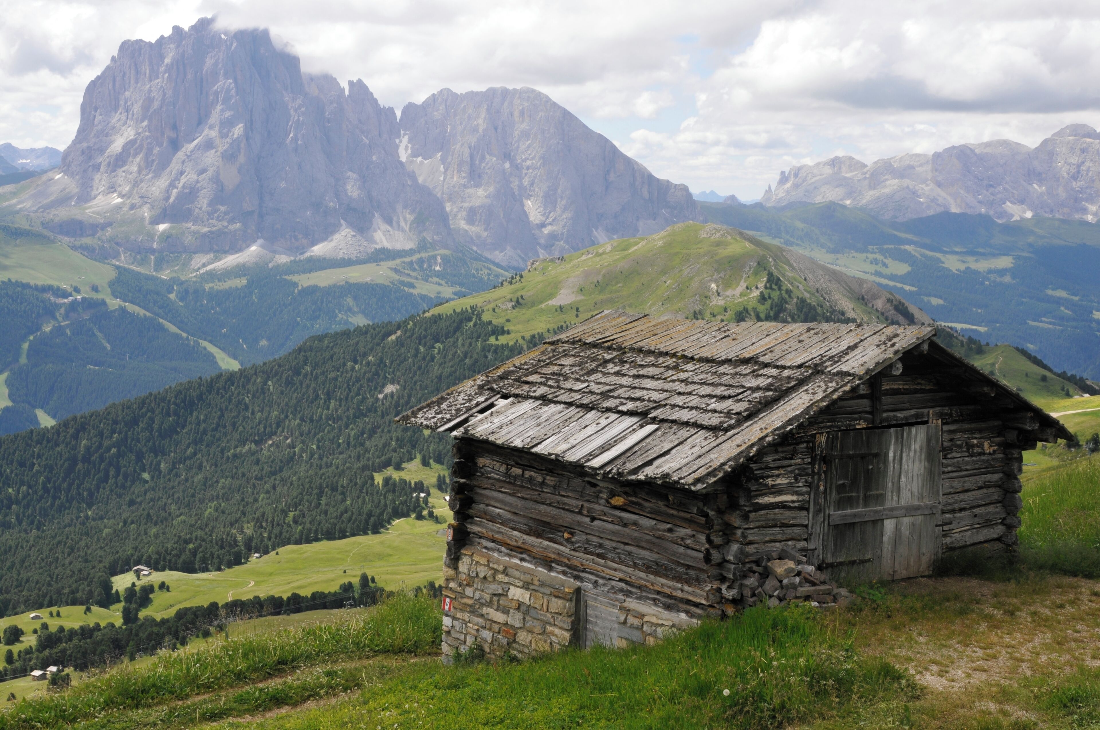 A rustic wooden cabin in a mountainous landscape with a prominent rocky peak in the background.
