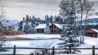 A wooden cabin in a snowy landscape with a fence in the foreground.
