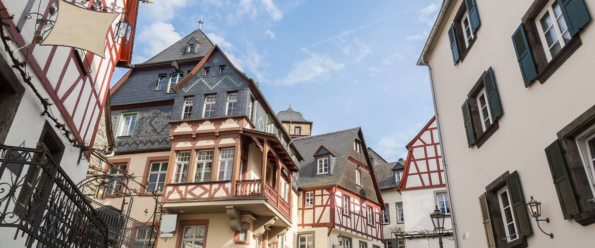 A narrow street lined with traditional half-timbered houses, a clear blue sky, and a white umbrella in the foreground.