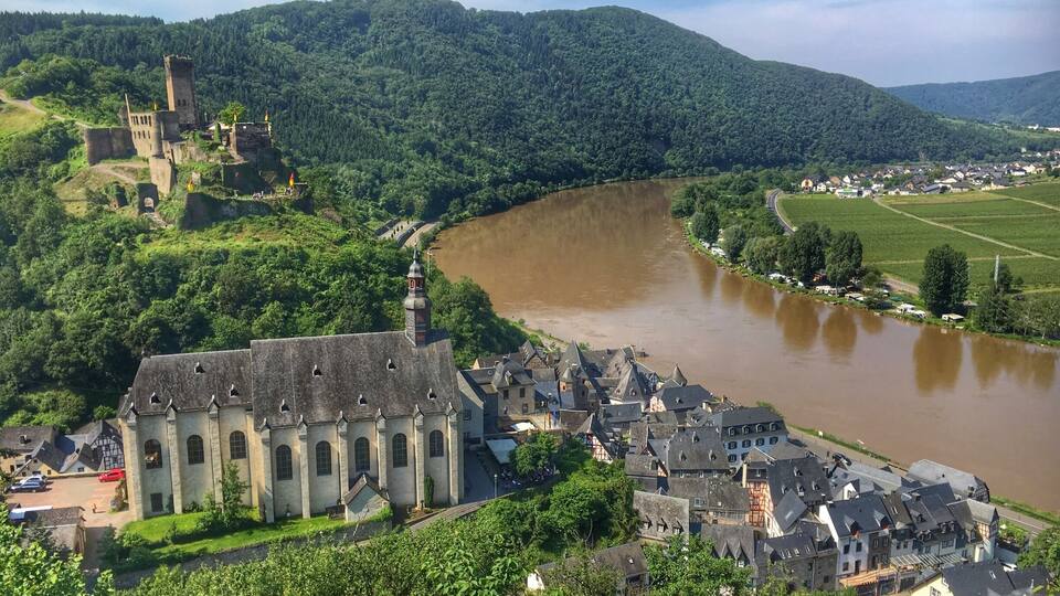 A river flowing through a town with a castle on a hill and lush greenery.