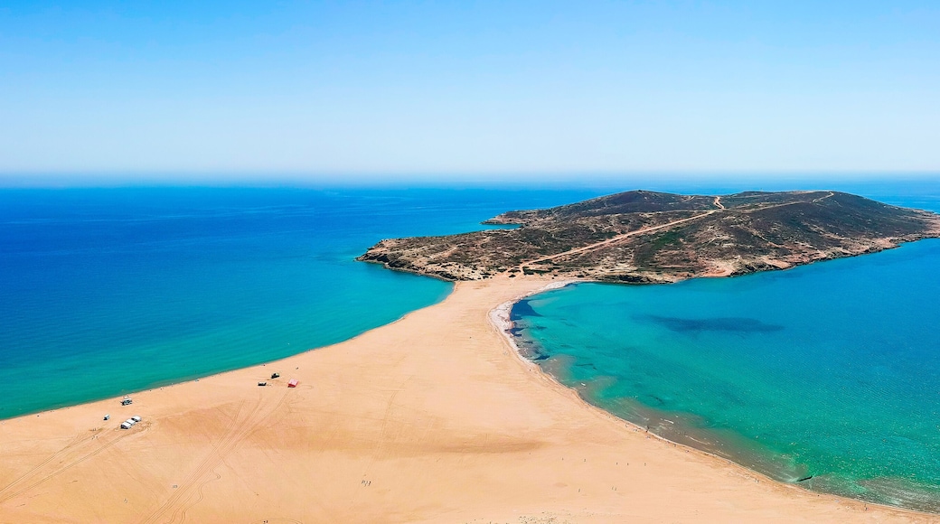 A coastal landscape with a sandy beach, clear turquoise waters, and a small island with a road leading to it.