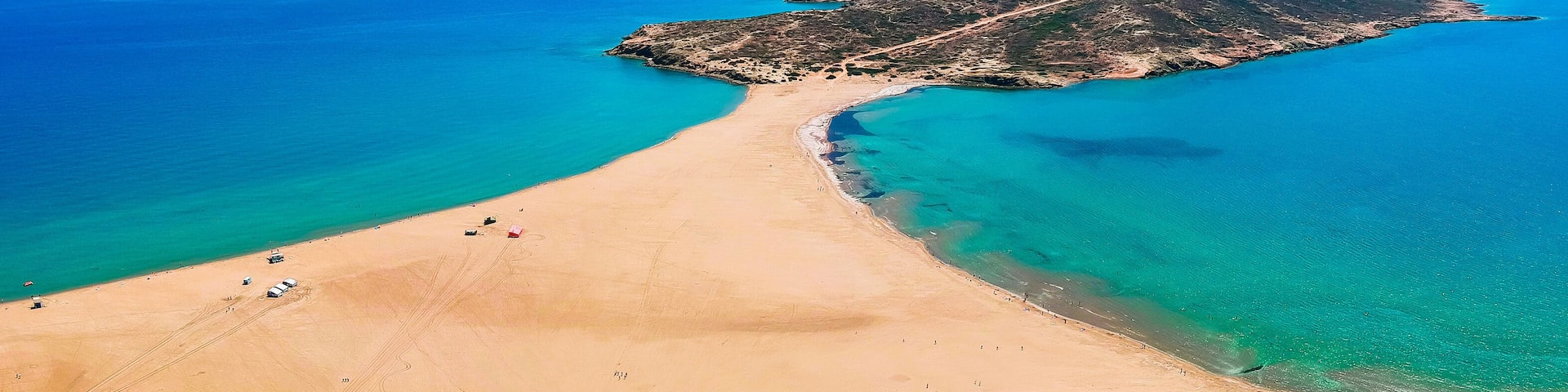 A coastal landscape with a sandy beach, clear turquoise waters, and a small island with a road leading to it.