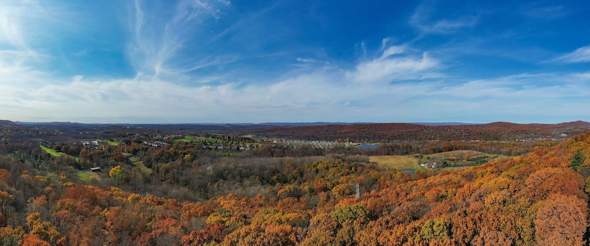 A valley with autumn foliage, a town in the distance, and rolling hills.