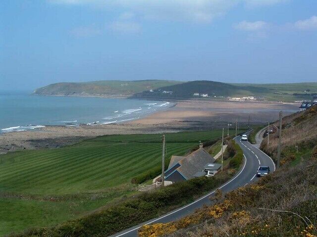 A coastal road with a beach, grassy fields, and a hilly landscape.