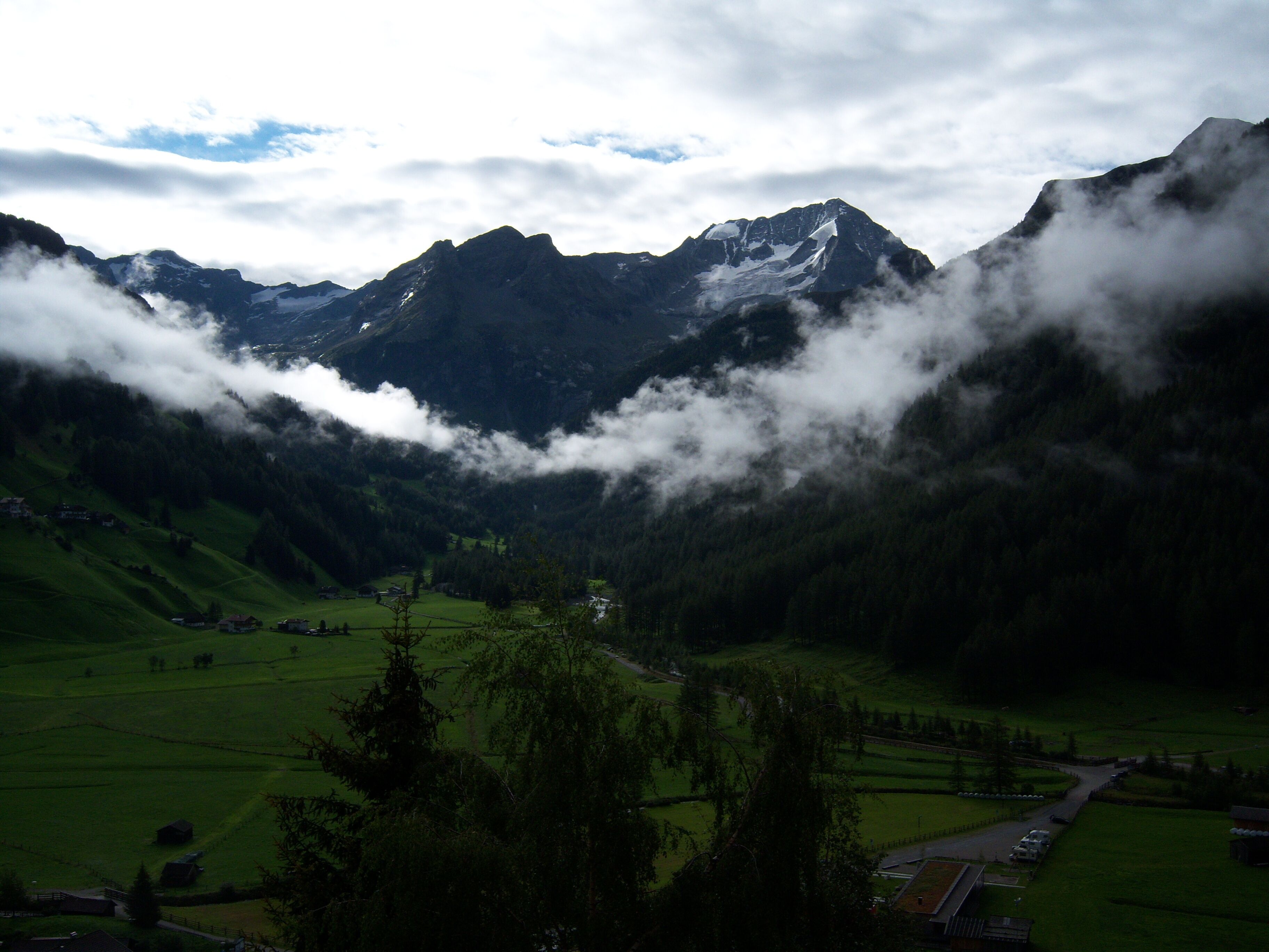A valley with green fields, a road, and snow-capped mountains in the background.