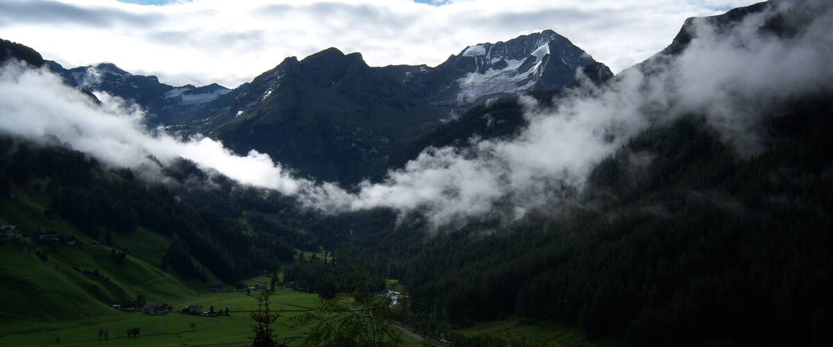 A valley with green fields, a road, and snow-capped mountains in the background.