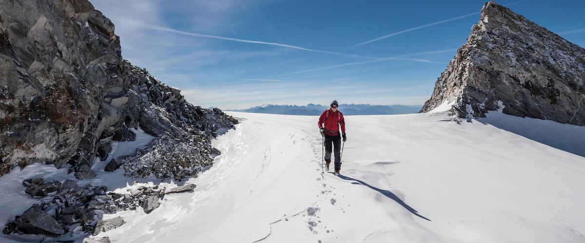 A person skiing on a snow-covered slope with rocky cliffs on either side and a clear blue sky.
