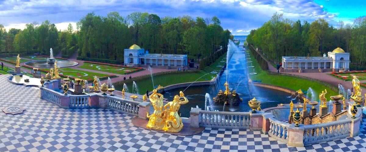 Un extenso jardín con una fuente central, estatuas ornamentales y un suelo a cuadros.