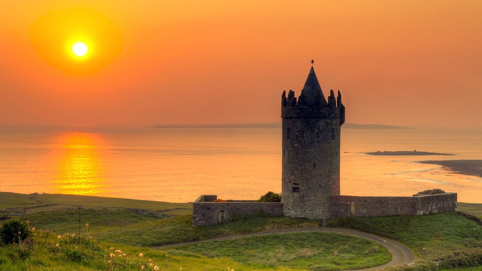A tower by a body of water during sunset.