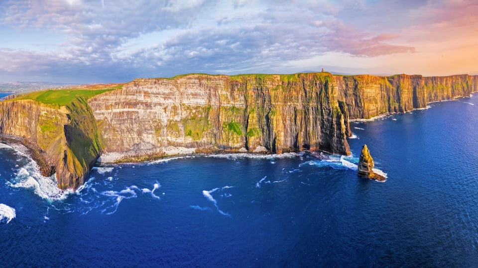 A coastal cliff with a lighthouse, ocean waves, and a clear sky.