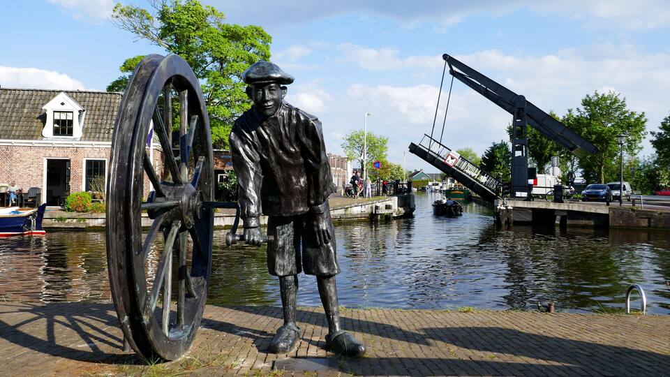 A statue of a man with a large wheel, a canal, and a bridge.