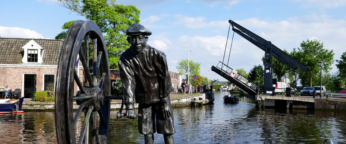 A statue of a man with a large wheel, a canal, and a bridge.