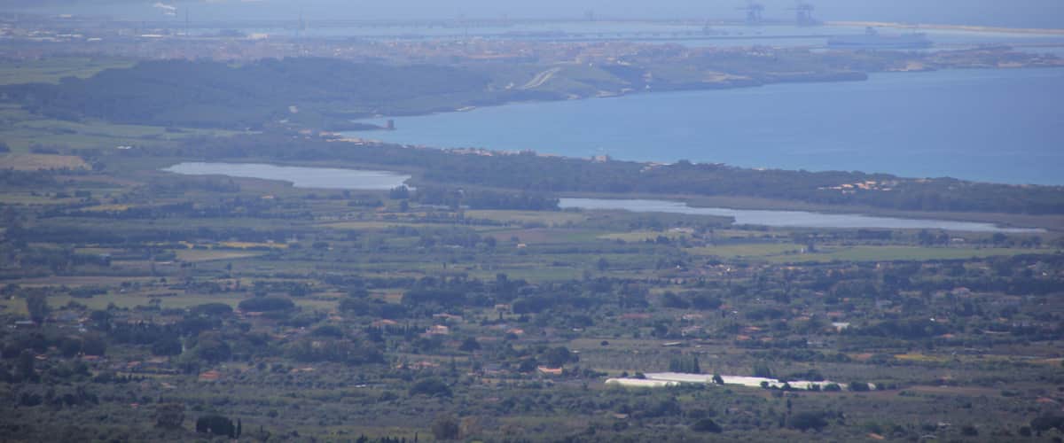 A coastal landscape with a large body of water, several small islands, and a distant industrial area.