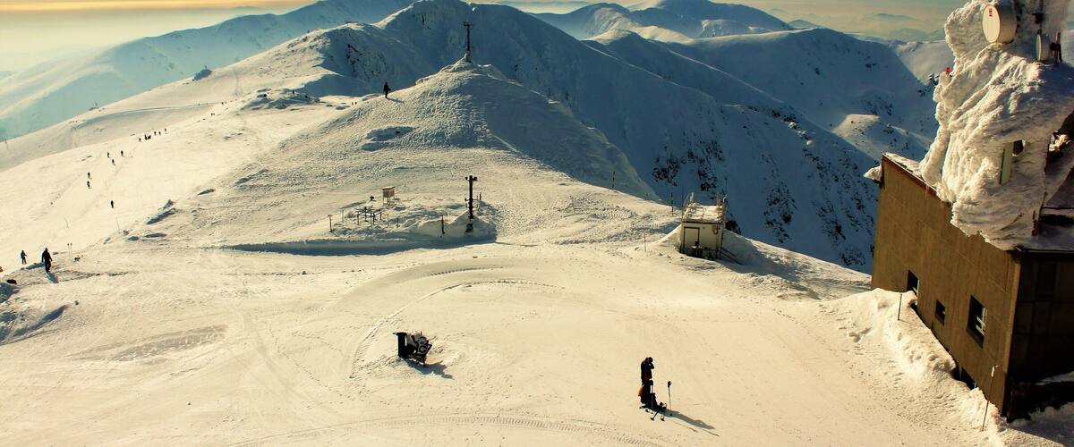 A snow-covered mountain landscape with ski trails, a ski lift, and a small cabin.
