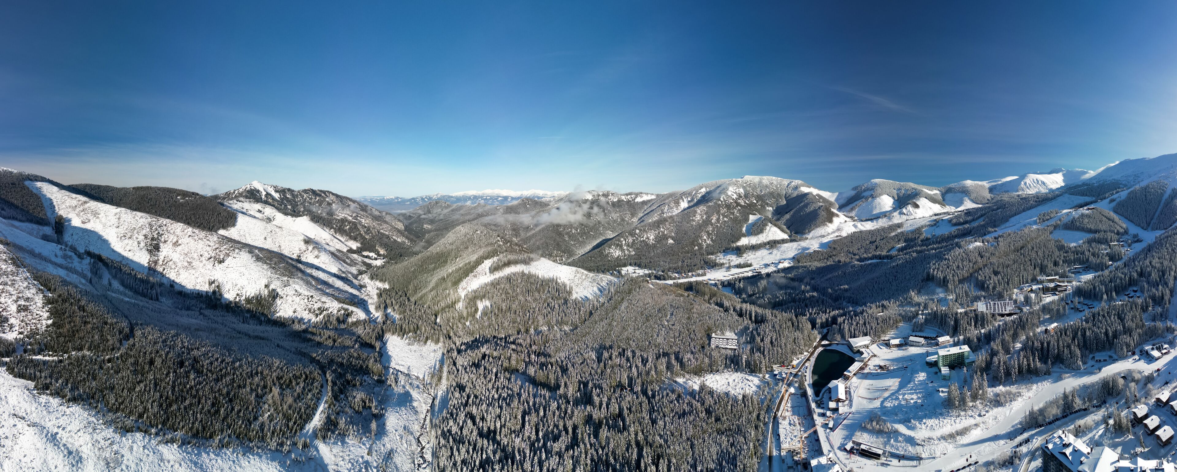 A snow-covered mountainous landscape with dense forests and a ski resort.