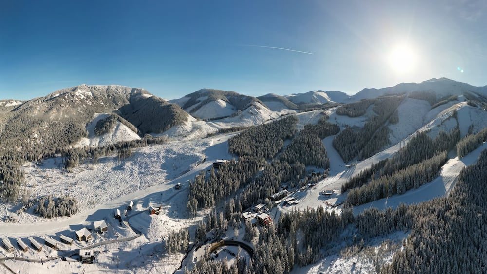 Aerial panoramic winter view of Demanovska Dolina village in Low Tatras mountains, Slovakia. Snowy overhead panorama of countryside rocky landscape with houses, scenic frozen pine forest and road