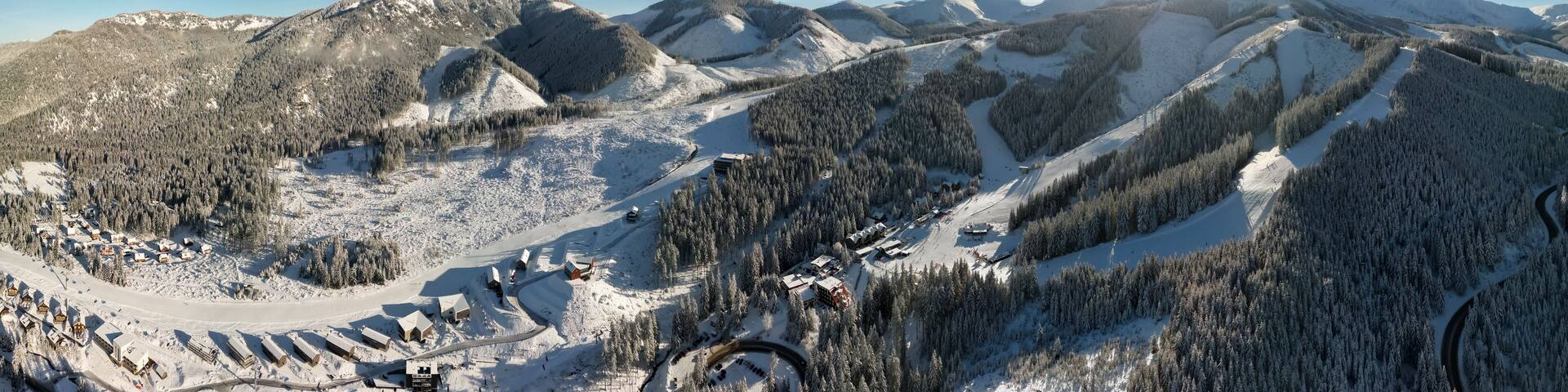 Aerial panoramic winter view of Demanovska Dolina village in Low Tatras mountains, Slovakia. Snowy overhead panorama of countryside rocky landscape with houses, scenic frozen pine forest and road