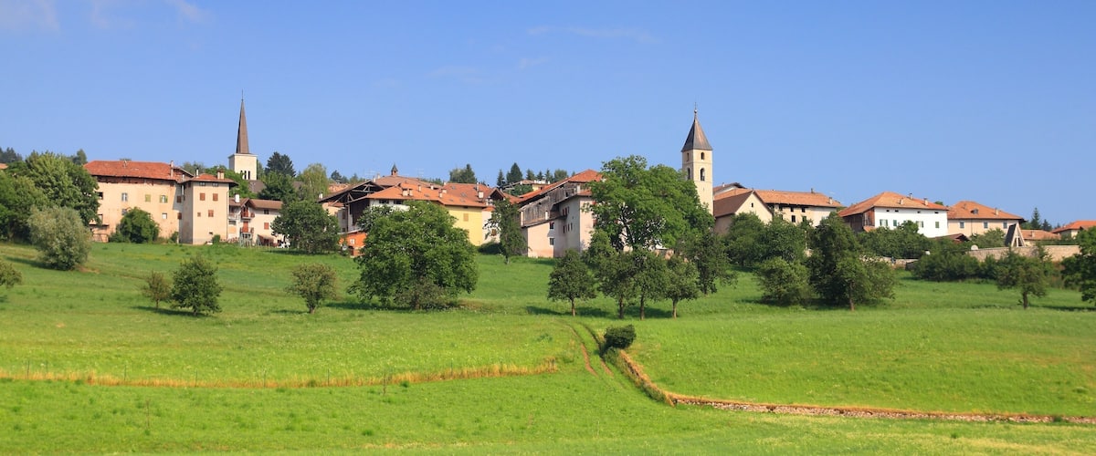 A town with a prominent church and a tall tower, surrounded by green fields and trees.
