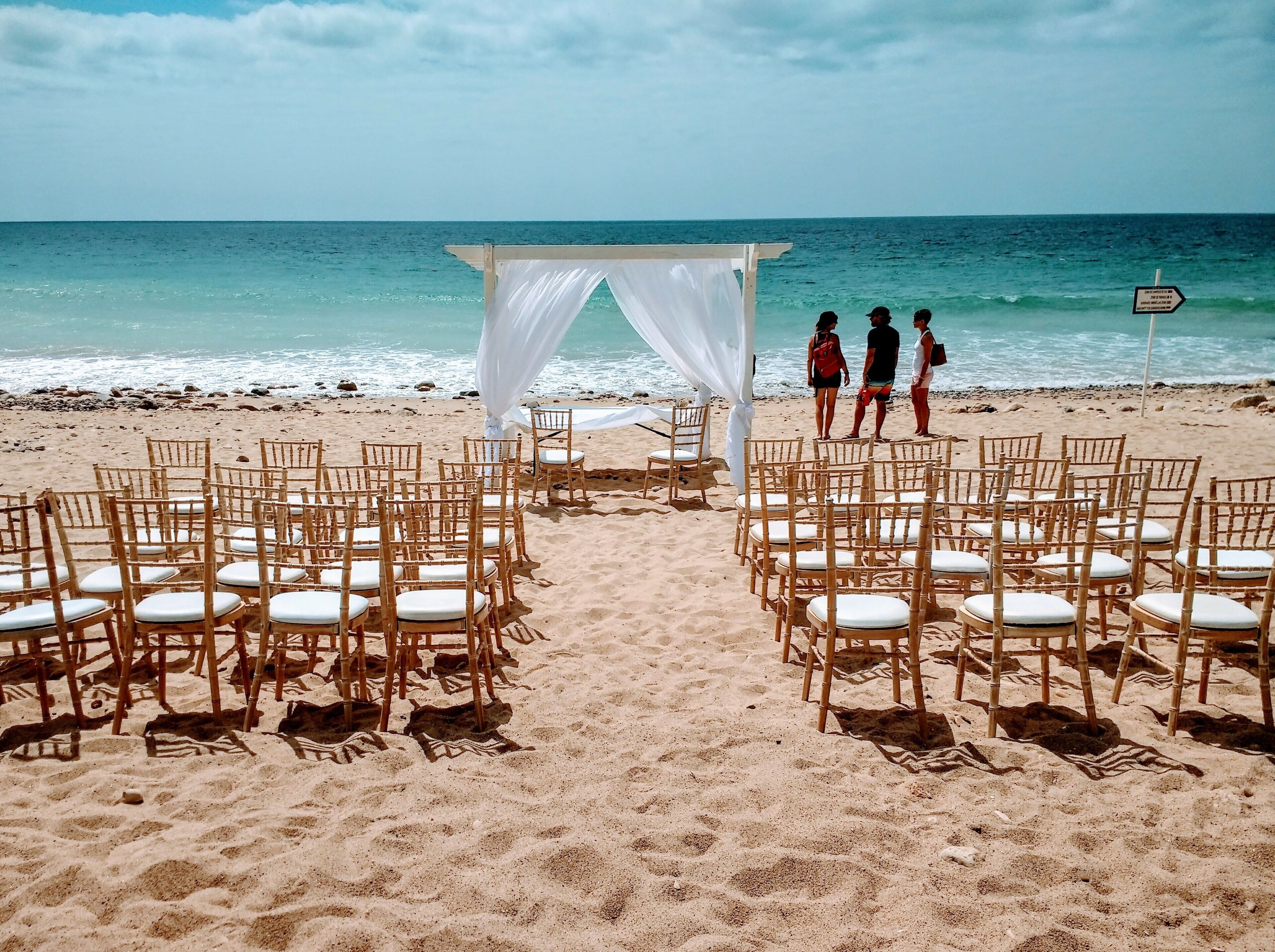 A beach ceremony setup with chairs and a white canopy.