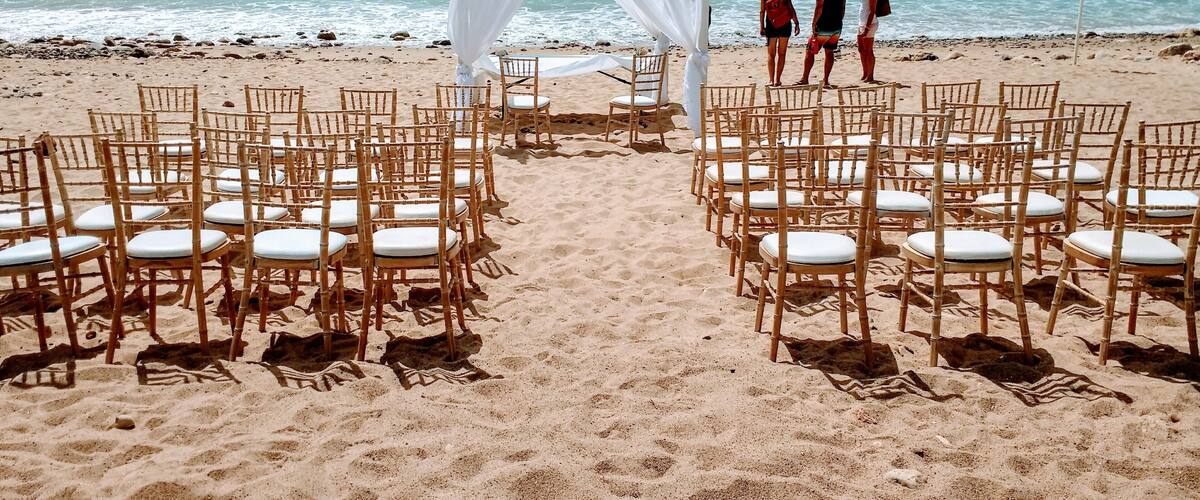 A beach ceremony setup with chairs and a white canopy.