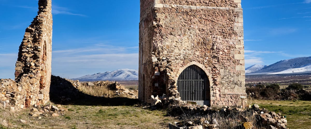 A stone church with a bell tower and a ruined pillar in a mountainous landscape.