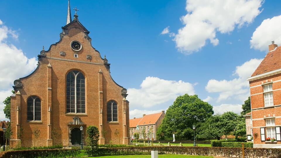 A historic church with a tall spire and a clock, surrounded by a well-maintained garden and other buildings.