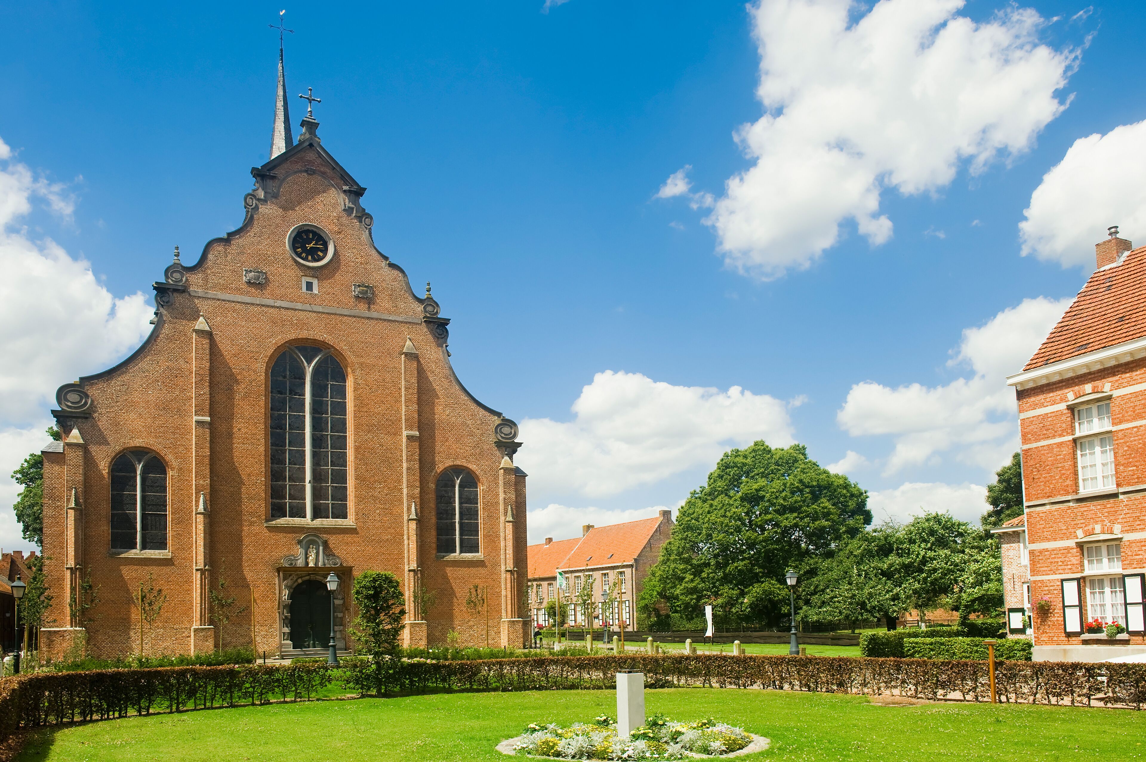 A historic church with a tall spire and a clock, surrounded by a well-maintained garden and other buildings.