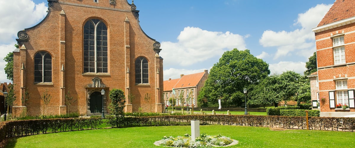 A historic church with a tall spire and a clock, surrounded by a well-maintained garden and other buildings.