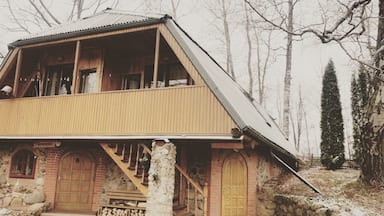 A wooden cabin with a sloped roof, stone foundation, and wooden doors.