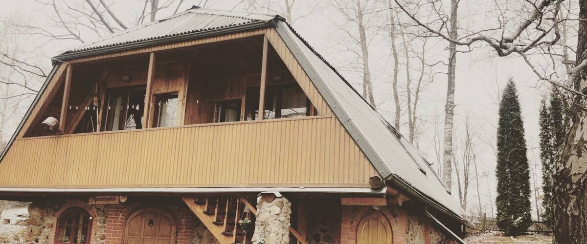 A wooden cabin with a sloped roof, stone foundation, and wooden doors.