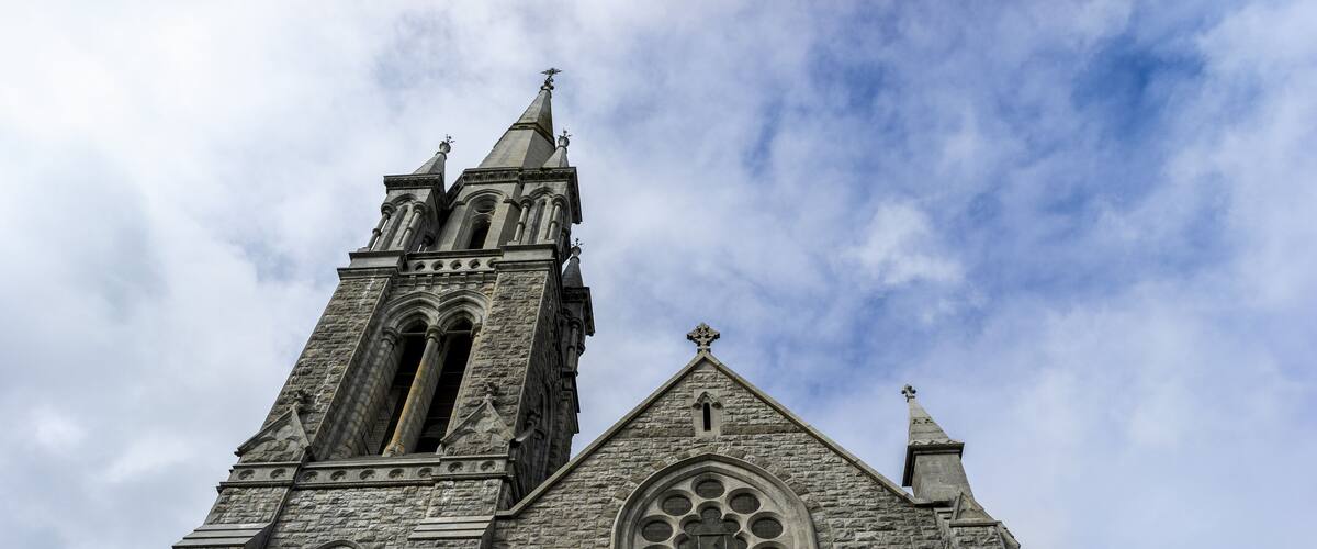 A stone church with a tall tower, large arched windows, and a cross at the top.