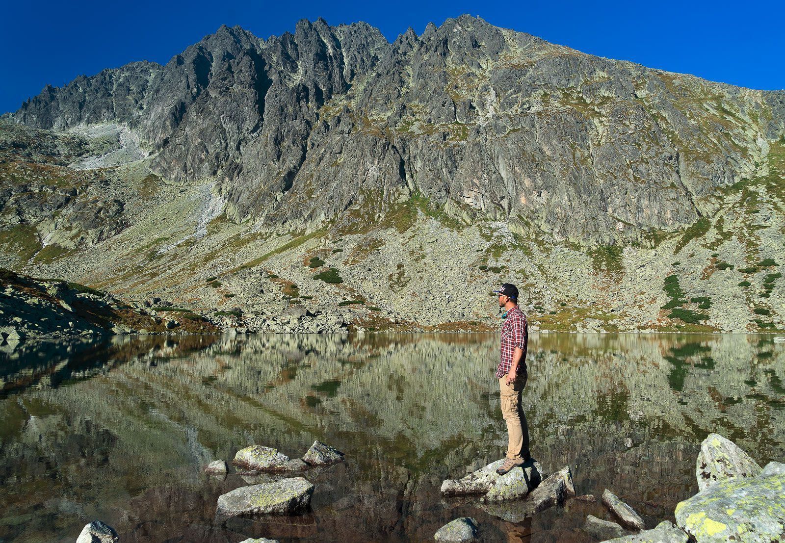 A person standing on rocks by a clear lake with a mountain in the background.