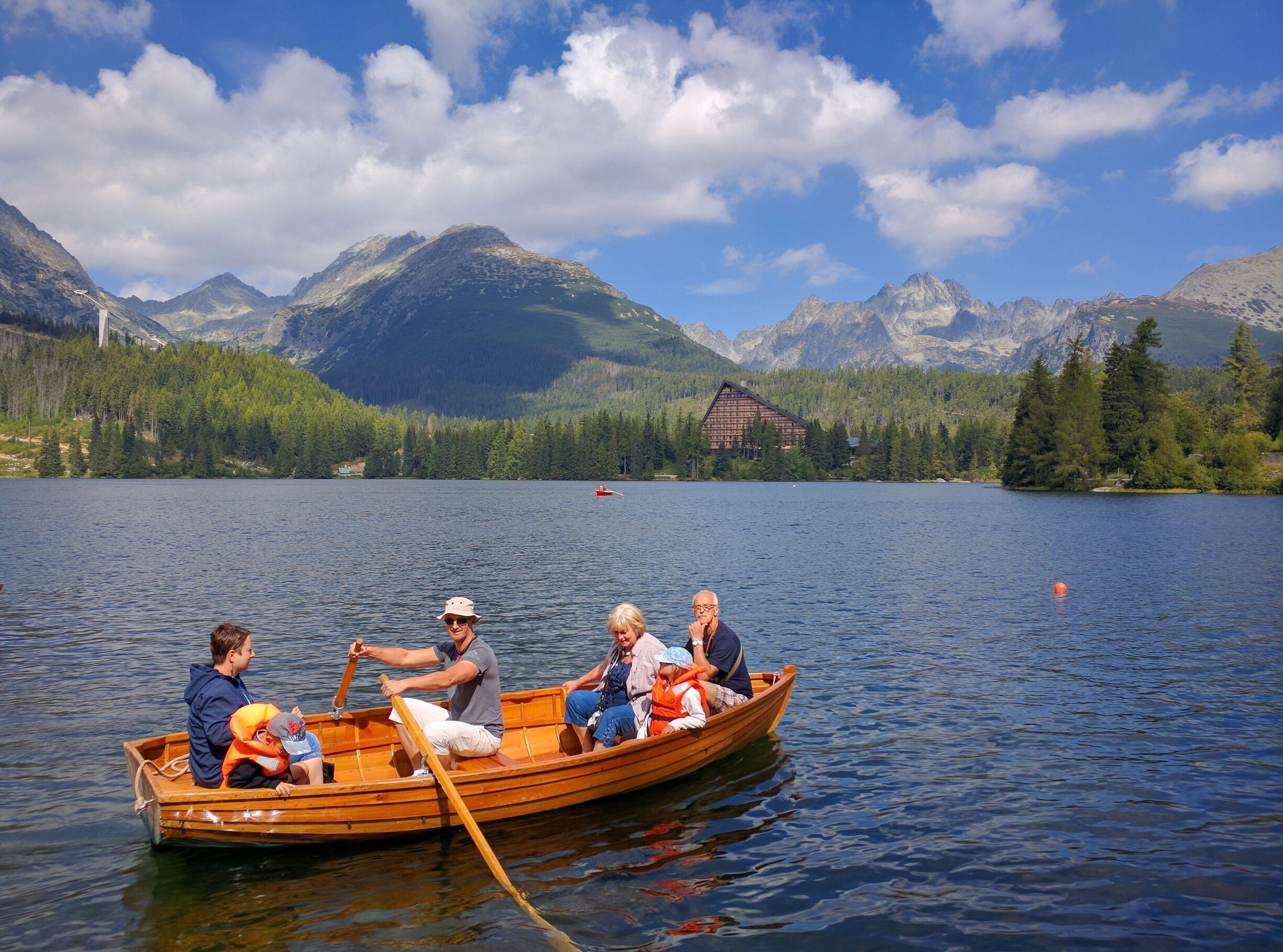 A group of people in a wooden boat on a calm lake with mountains in the background.