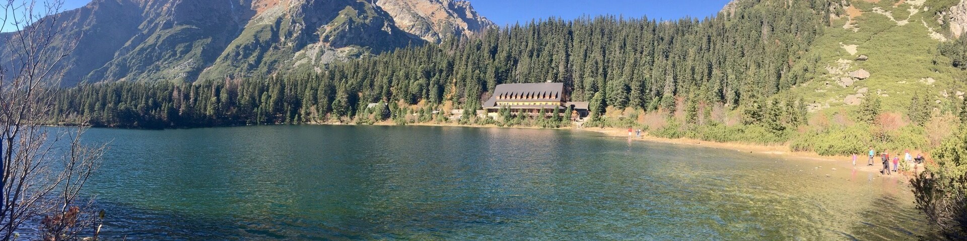 Un lago de montaña con una cabaña rodeada de un bosque denso y montañas rocosas.