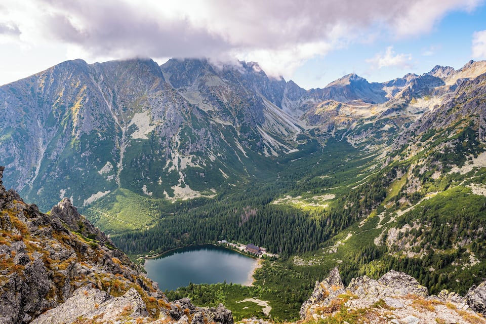 Un paisaje montañoso con un lago y un pequeño edificio.