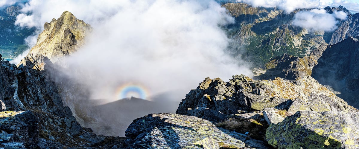Een bergtop met een regenboog en wolken.