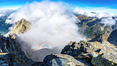 Pico de montanha com arco-íris e nuvens.