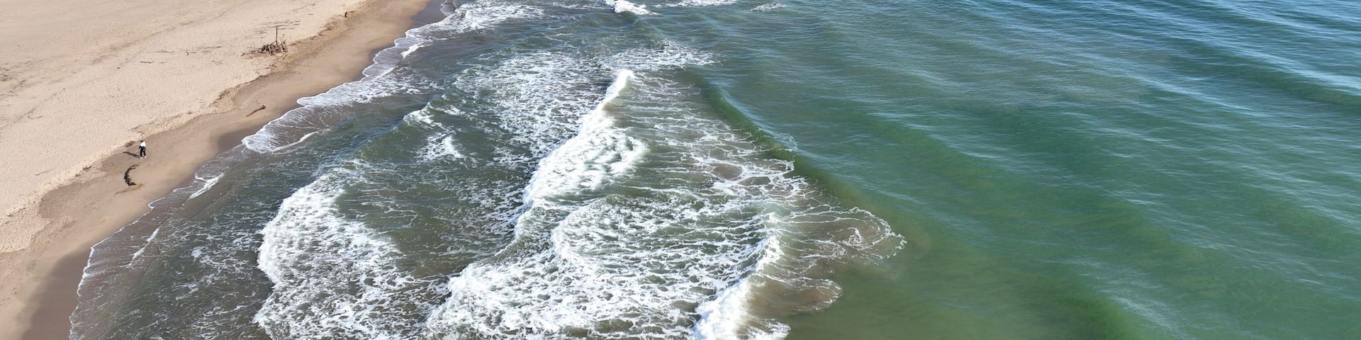 A sandy beach with waves crashing onto the shore, a clear sky, and a distant city skyline.