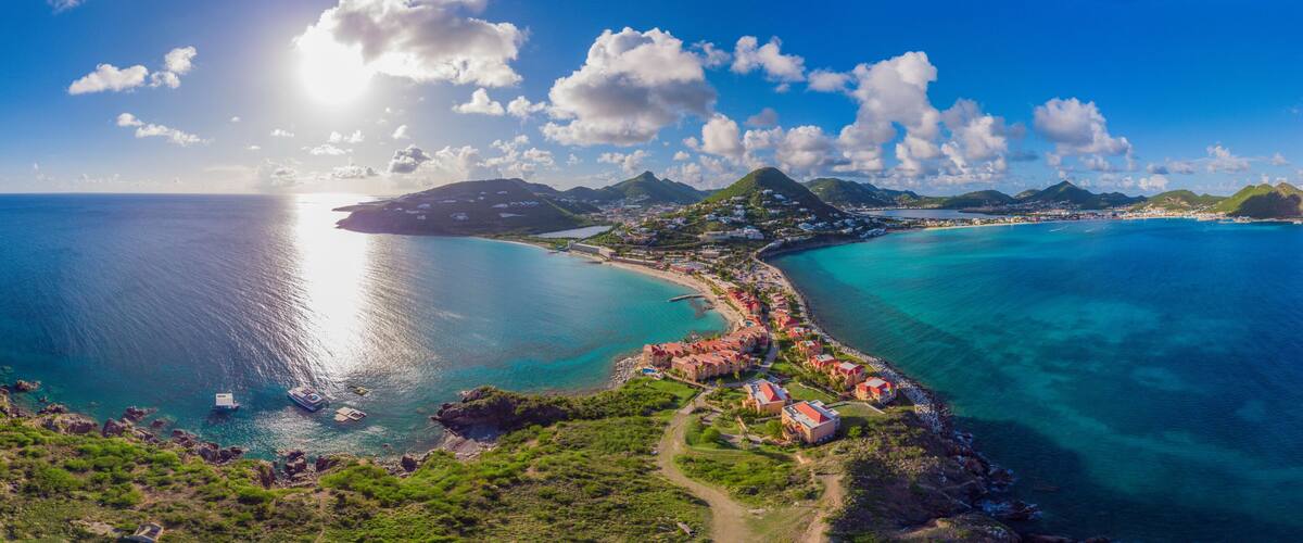 A coastal town with a clear blue sea, a winding road, and a mountainous backdrop.
